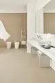 Weißes Badezimmer mit minimalistischer Einrichtung. Zwei Sanitäranlagen, ein Waschbecken auf einer langen Ablage und ein Spiegel. Handtücher auf einer Leiter. Ideal Standard Produkte sind erkennbar.